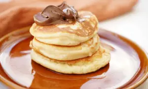 En stapel fluffiga amerikanska pannkakor toppas med chokladkräm på en brun tallrik.