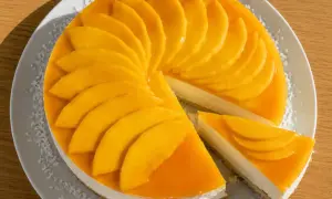 En krämig mango cheesecake med färska mangoskivor som pryder toppen. En bit är uppskuren och visar den lena fyllningen.