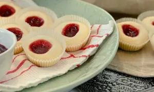 Glutenfria hallongrottor med sylt på en ljusgrön tallrik, bredvid en skål med hallonsylt och en sked.