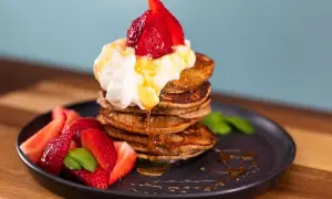 En stapel bananpannkakor med vispgrädde, jordgubbar och sirap. Ett perfekt bananpannkaka recept för frukost eller brunch.