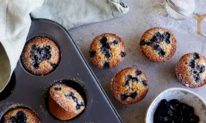 Nybakade blåbärsmuffins, en klassisk financier kaka, ligger i en form bredvid en skål med sylt och en sil.
