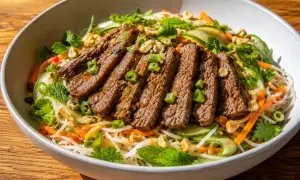 En läcker asiatisk biffsallad med tunt skivad biff, nudlar, gurka, morötter, mynta och jordnötter i en skål.