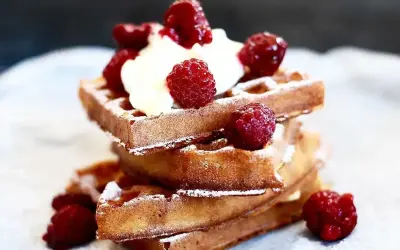 En stapel gyllene belgiska våfflor toppade med vispad grädde och färska hallon, pudrade med florsocker. En härlig frukost eller dessert.