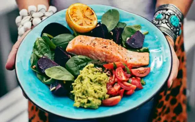 En matig sallad med lax, avokado, rödbetor, tomater och citron på en turkos tallrik.