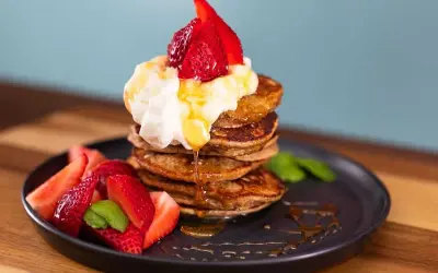 En stapel bananpannkakor med vispgrädde, jordgubbar och sirap. Ett perfekt bananpannkaka recept för frukost eller brunch.
