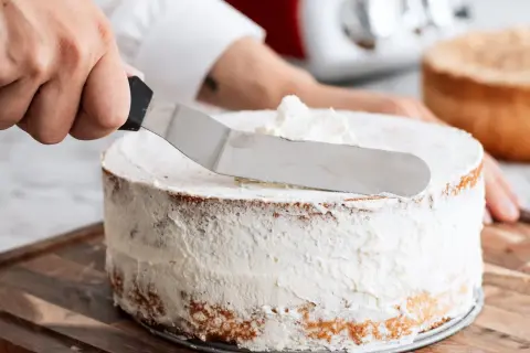 En hand sprider fluffig grädde på en tårta, en del av enkla tårtfyllningar.