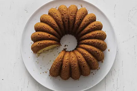 En gyllene sockerkaka med kardemumma, med en bit borttagen, ligger på en vit tallrik.