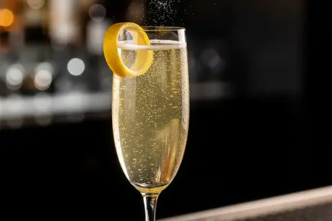 Ett glas French 75 med bubblor och en citronskal.