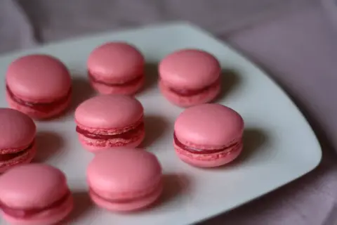 Rosa macarons med fyllning på en vit tallrik. Perfekt för ett macarons recept.