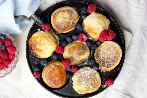 Små, gyllene pannkakor med pudersocker och bär, redo att avnjutas. Ett perfekt krabbelurer recept för frukost eller fika.