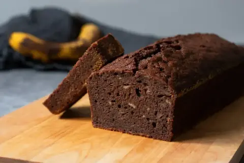 En saftig banankaka i sockerkaksform, med en skiva upplagd. En övermogen banan ligger i bakgrunden.