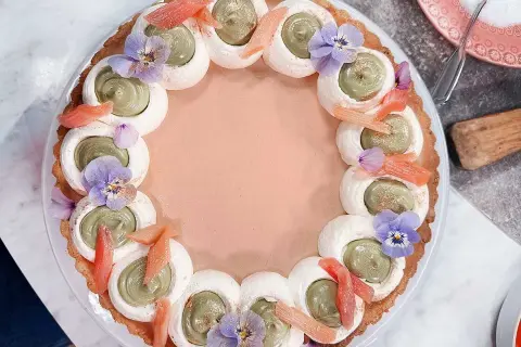 En vacker pannacotta med rabarber, dekorerad med grön kräm, maräng, violer och rabarberbitar.