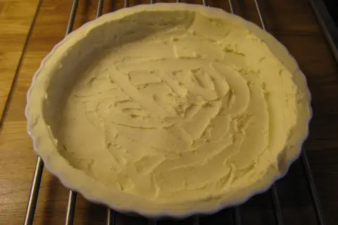 En ljusgul, krämig glutenfri pajdeg i en vit pajform, redo att fyllas.