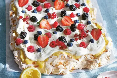En stor pavlova med lemoncurd, toppad med vispgrädde och färska bär som jordgubbar, hallon, blåbär och vinbär.