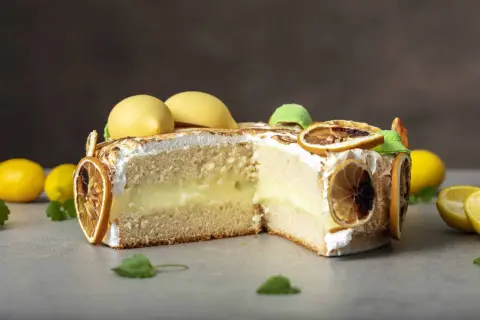 En skivad citron tarte med fluffig maräng, krämig fyllning och dekorerad med torkade citronskivor och gula marängkulor.