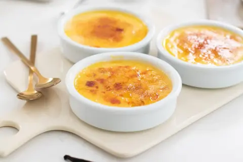 Tre krämiga crème brûlée i vita skålar med karamelliserat socker. Perfekt för ett enkelt creme brulee recept.