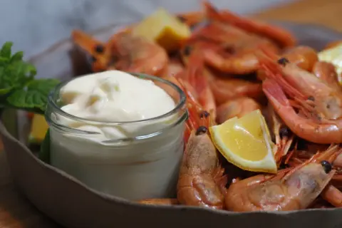 En skål med räkor och citronklyftor, med en liten burk krämig aioli. Perfekt för ett enkelt aioli recept.