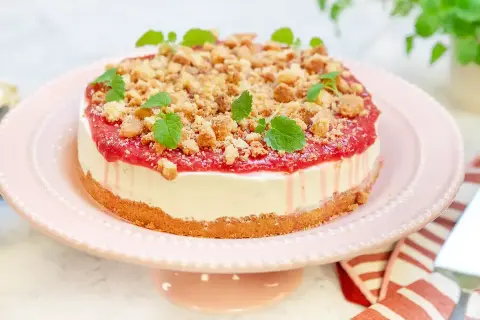 En läcker rabarber cheesecake med smulig topping och myntablad, serverad på ett rosa tårtfat.