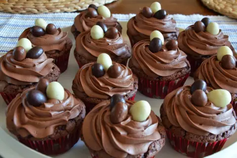 En bricka med chokladmuffins med krämig choklad frosting, dekorerade med små chokladägg i olika färger.