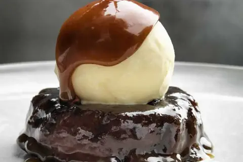 En läcker sticky toffee pudding med en kula vaniljglass och varm kolasås som rinner över.