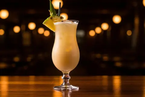 En krämig alkoholfri pina colada med ananasskiva och blad som dekoration, serverad i ett elegant glas på en träyta.