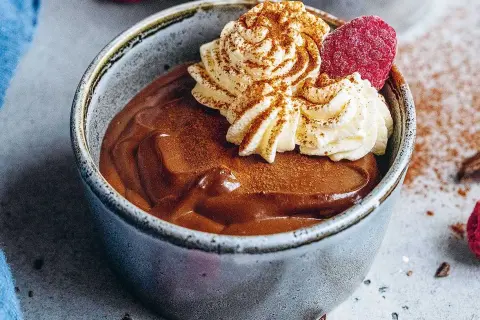 En krämig chokladpudding i en skål, toppad med vispad grädde, hallon och kanel. Perfekt för ett chokladpudding recept.