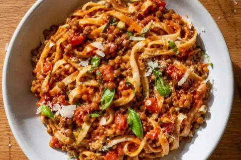 En skål med tagliatelle täckt av en mustig vegetarisk pastasås med linser, tomater och basilika, toppad med parmesan.