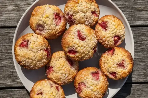 En tallrik med fluffiga muffins med jordgubbar, toppade med socker och citronskal. Perfekta för fika!