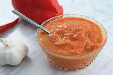 En skål med ajvar relish, en röd paprika, en chili och ett vitlökskläpp.