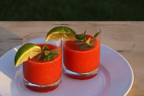Två glas med fryst jordgubbsdaiquiri, garnerade med lime och mynta. Perfekt för ett somrigt strawberry daiquiri recept.