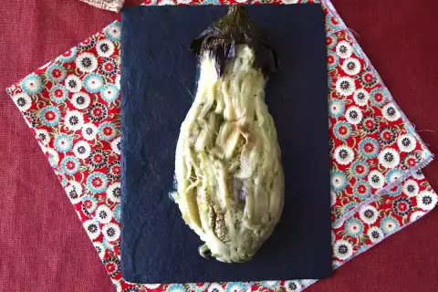 En ugnsbakad aubergine, mjuk och saftig, serveras på en svart skifferplatta.