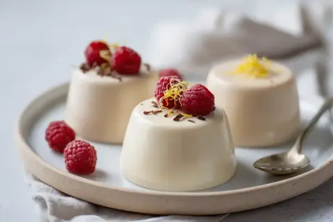 Tre krämiga panna cotta-desserter med hallon och citronskal på en tallrik.