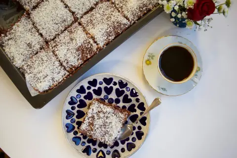 En saftig citronkaka i långpanna, toppad med kokosflingor, serveras med en kopp kaffe.