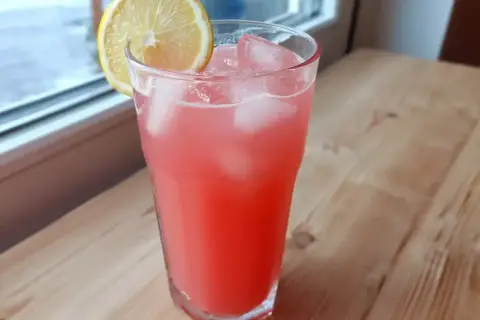 Ett glas rosa rabarberlemonad med is och en citronskiva, redo att avnjutas.