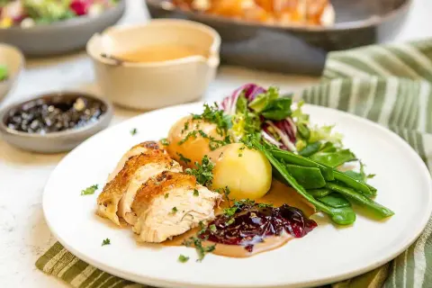 En saftig hel kyckling i ugn, skuren och serverad med potatis, sockerärtor och en härlig lingonsylt.