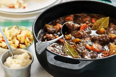 En mustig kalops med morötter och lagerblad i gjutjärnsgryta, serverad med äppelkompott och potatismos. Ett klassiskt kalops recept.