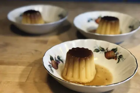 Tre krämiga creme caramel i vackra skålar med fruktmotiv. En härlig dessert som väntar.
