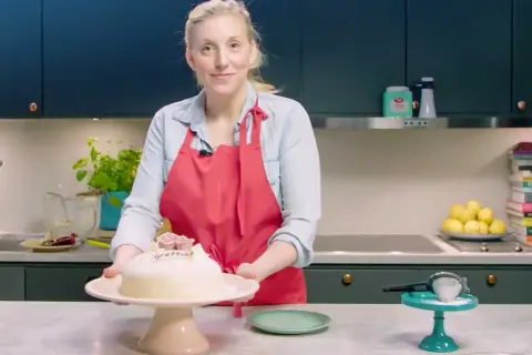 Kvinna med röd förkläde presenterar en marsipantårta. Ett perfekt marsipan recept för firande.