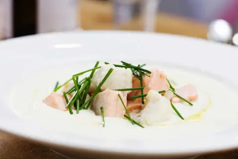 En krämig soppa med bitar av confiterad lax och vit fisk, toppad med färsk gräslök.