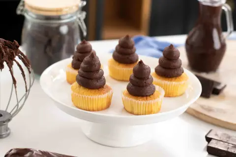Fem cupcakes med chokladganache, perfekt för ett enkelt ganache recept. Ingredienser för bakning syns i bakgrunden.
