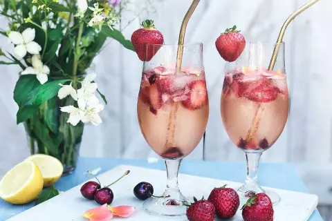 Två glas med drink med gin och prosecco, fyllda med is, jordgubbar och körsbär. Garnerade med jordgubbar och serverade med citroner och blommor.