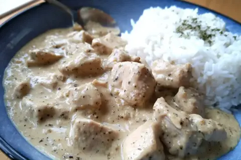 En krämig sås till kyckling och ris, med bitar av kyckling i en len sås. Riset är toppat med lite grön krydda.