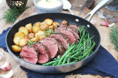 Helstekt oxfilé, saftig och perfekt rosastekt, serveras med krispiga haricots verts och gyllene potatisar i en stekpanna. En festmåltid!