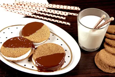 S'mores i ugn: tre chokladöverdragna kex med marshmallowfyllning på en prickig tallrik, bredvid ett glas mjölk och fler kex.