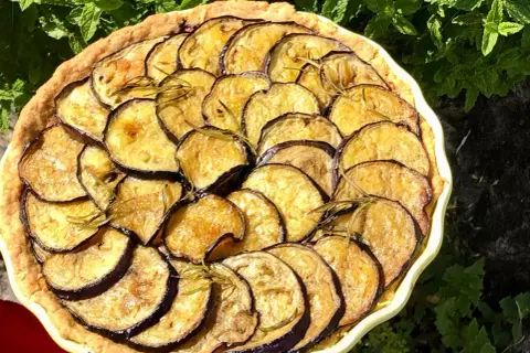 En paj med gyllene, stekt aubergine och rosmarin, vackert arrangerad i en ljusgul form.
