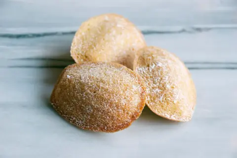 Tre gyllene madeleines, pudrade med florsocker, redo att avnjutas. Ett enkelt och gott madeleine recept.