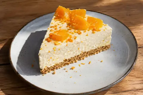 En bit krämig apelsincheesecake med kexbotten, toppad med apelsinklyftor och rivet skal. Ett perfekt cheesecake recept för fikat.