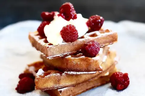 En stapel gyllene belgiska våfflor toppade med vispad grädde och färska hallon, pudrade med florsocker. En härlig frukost eller dessert.