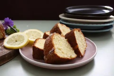 Skivor av saftig citron sockerkaka på en ljusrosa tallrik, med citronskivor och en lila blomma som dekoration.