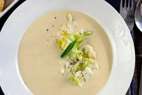 Krämig potatis och blomkålssoppa med garnering av blomkål, salladslök och peppar. Serveras med en bit rostat bröd.